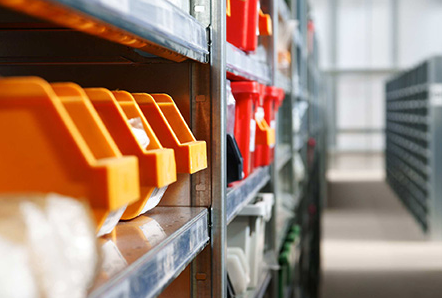 Organized stockroom shelving with labeled orange and red parts bins